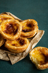 Pile of traditional Portuguese pastel de nata on paper bag on green surface.