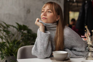 Happy young woman sitting on sofa in cafe or restaurant. Portrait of comfortable woman in sweater...
