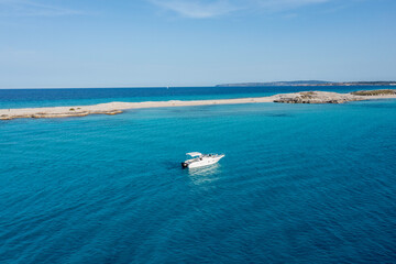A yacht floating on the beautiful blue waters of Formentera, with a couple lying down and resting on board.