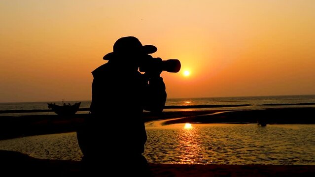Silhouette of the photographer standing on the camera's shoulder in front of the ocean at sunset. Silhouette and back views of a travel photographer.
