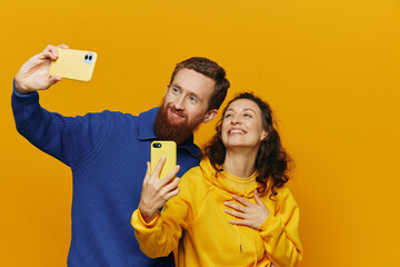 Man and woman couple smiling merrily with phone in hand social media viewing photos and videos, on yellow background, symbols signs and hand gestures, family freelancers.