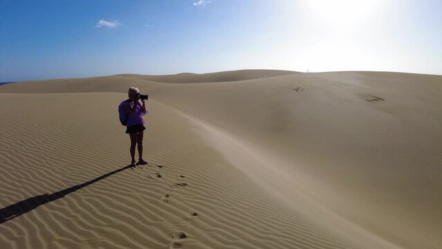 Photographer woman visiting the Maspalomas Dunes of Gran Canaria walks through the rolling sand dunes, she might stop to take photos of the stunning scenery or to observe the local wildlife.