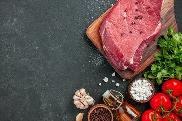 top view raw meat slice with greens and red tomatoes on a dark background cooking dish food meat dinner meal butcher barbecue color