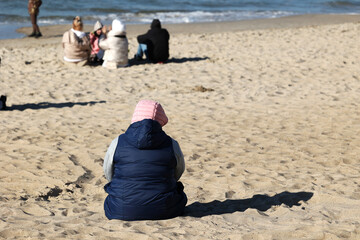 Ciepło ubrani ludzie na plaży nad morzem wiosną.  - obrazy, fototapety, plakaty