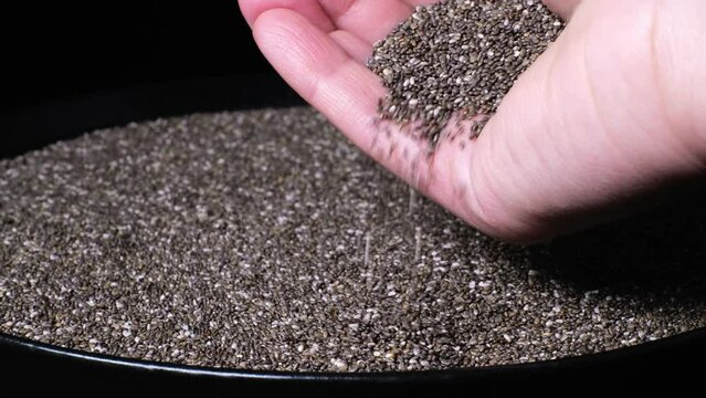 Slow motion of female hand holding beautiful natural dried chia seeds. Close-up of organic black and white Salvia Hispanica seeds falling down. Healthy superfood, rich in Omega 3 fatty acids. 4K