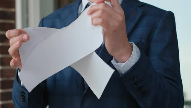 Irritated man in a business suit breaks the contract into pieces, close-up