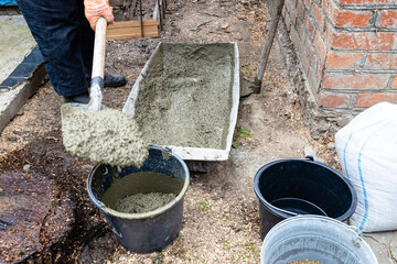 builder puts concrete in bucket with shovel in backyard in village outdoors