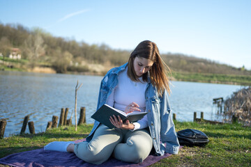 Woman at lakeside writing in a notebook. Nature concept. Self reflection.