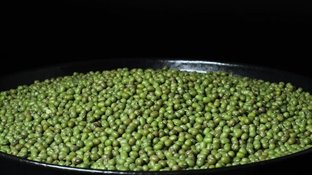 Close-up of organic natural dried green mung beans (Vigna radiata) rotating on a plate. Green gram or maash beans with black copy space. Concept of healthy lifestyle, vegetarian or vegan food diet.