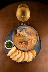 seafood soup with New Zealand mussel toast and green spring onion on wooden table portrait with glass of white wine topview