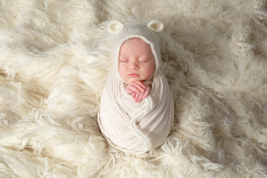 white background, care concept. newborn baby is sleeping. photo of a baby sleeping on a white blanket in a cute hat with teddy bear ears