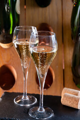 Glasses of sparkling white wine champagne or cava with bubbles and classic wooden champagne pupitre rack with empty bottles on background