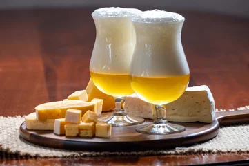 Gordijnen Glasses of Belgian light blonde beer made in abbey and wooden board with variety of belgian cheeses © barmalini