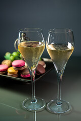 Glasses of sparkling white wine champagne or cava with bubbles and sweet dessert colorful macarons biscuits on background