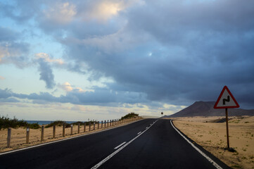 Driving car on black asphalt road through white sandy dunes near Corallejo beach on sunset Fuerteventura, Canary islands, Spain