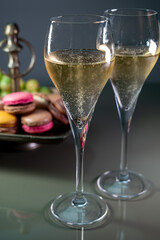 Glasses of sparkling white wine champagne or cava with bubbles and sweet dessert colorful macarons biscuits on background