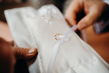 Obraz na płótnie Canvas Anelli di matrimonio d'oro serviti su un cuscino bianco e fiocchi bianchi