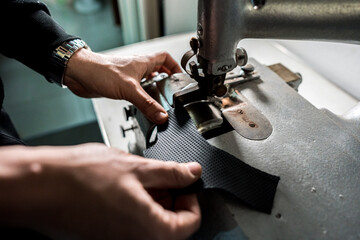 Mani di tappezziere che lavora un pezzo di stoffa e pelle su una macchina  in una industria tessile - obrazy, fototapety, plakaty