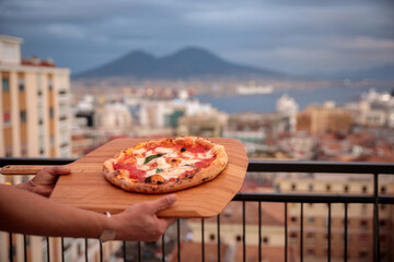 Pizza Napoletana offerta su un vassoio di legno con il Vesuvio e la città di Napoli alle spalle