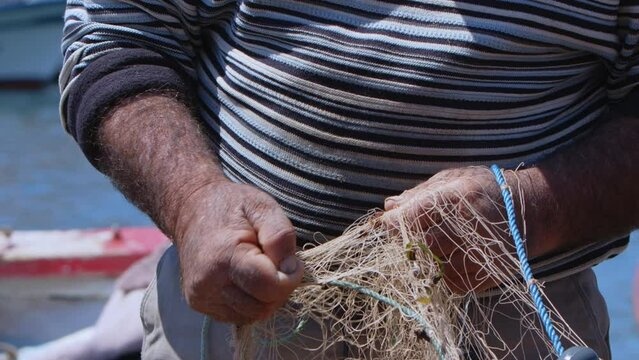 Fisherman is Repairing Fishnets on Fishing Boat in Dock