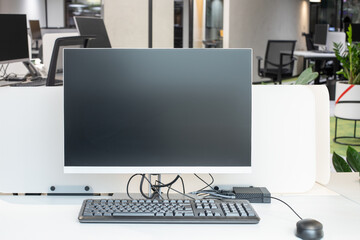 Desktop computer with a black LCD monitor on a white office desk, next to a keyboard and mouse, a modern office