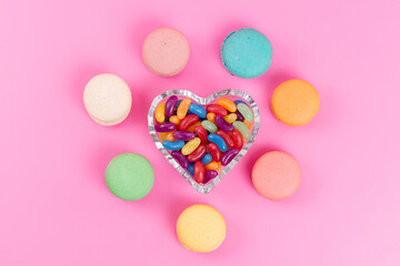 a top view french macarons round lined along with chewing candies on the pink background cake sweet sugar