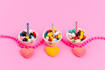 a top view multicolored candies inside white paper packages along with candles and marmalade on the pink desk color rainbow sugar sweets