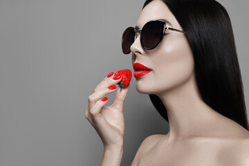 Attractive woman in stylish sunglasses holding strawberry on grey background, space for text. Color...
