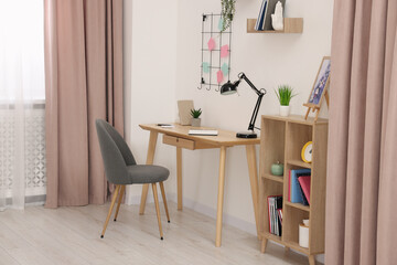 Stylish workplace with wooden desk, chair and lamp in room. Interior design