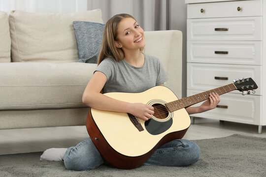 Teenage girl playing acoustic guitar near sofa in room