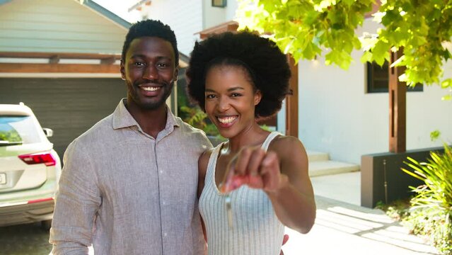 Portrait of couple at outside new home holding up keys to camera on moving day - shot in slow motion