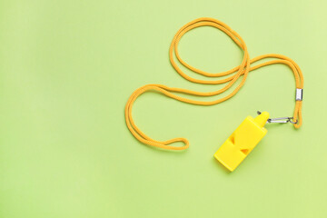 One yellow whistle with cord on light green background, top view. Space for text