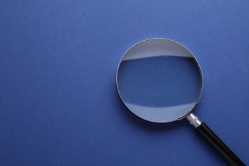 Magnifying glass on blue background, top view. Space for text