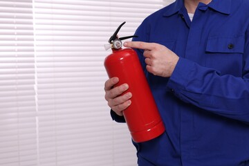 Man checking pressure and quality of fire extinguisher indoors, closeup. Space for text
