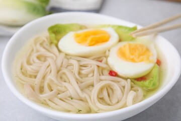 Bowl of delicious rice noodle soup with celery and egg on light grey table, closeup