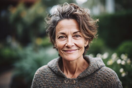 Close-up portrait photography of a grinning woman in her 50s wearing a cozy sweater against a botanical or butterfly garden background. Generative AI
