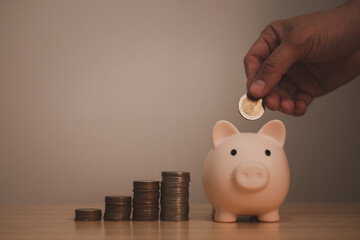 piggy bank with hand of a man under saving coin in piggy bank, symbol of saving for future investment or retirement by small deposit money continuously