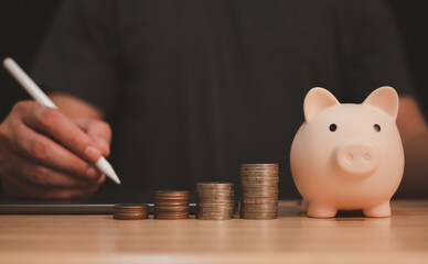 a man using tablet to record money with piggy bank and saving coin in front of him, money management is one of the key to success in financial freedom