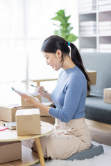 Asian business woman on sofa using a laptop computer checking customer order online shipping boxes at home. Starting SME Small business entrepreneur freelance. Online business, SME Work home concept.
