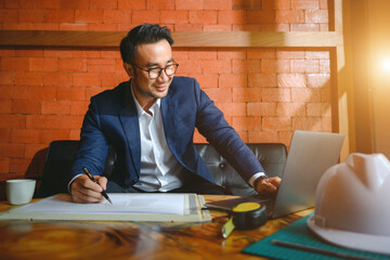 Asian male business boss using a notebook computer with engineer blueprint Succeed in business. business planning concept