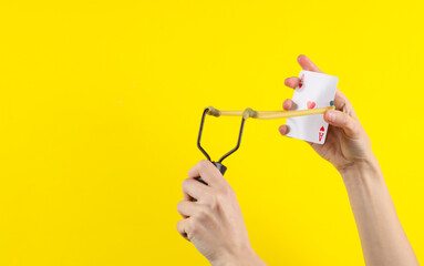 Hands holding slingshot with ace of hearts on a yellow background.