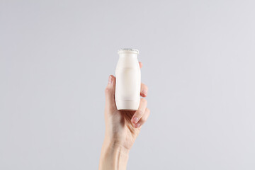 Female hand holding a bottle of yogurt on a gray background