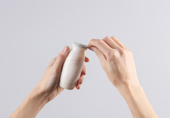 Female hands open a bottle of yogurt on a gray background