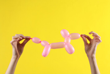 Woman's hands holding a pink balloon in the shape of dog on yellow background