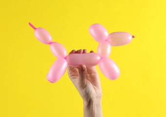 Woman's hand holding a pink balloon in the shape of dog on yellow background