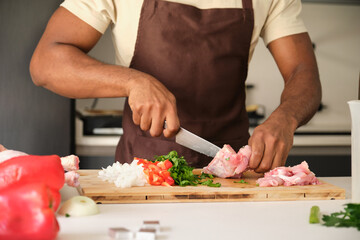 Obraz na płótnie Canvas Unrecognizable young black man de-boning chicken to prepare a recipe in a kitchen.
