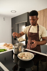 Young black man preparing boiled chicken mince with vegetables recipe in a kitchen.