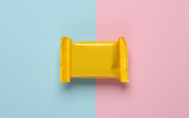 Yellow candy packaging on a blue-pink pastel background. Top view