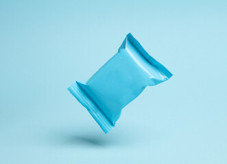 Blue candy packaging levitating on blue background with shadow.