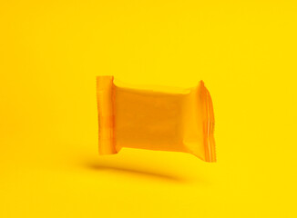 Yellow candy packaging levitating on yellow background with shadow.